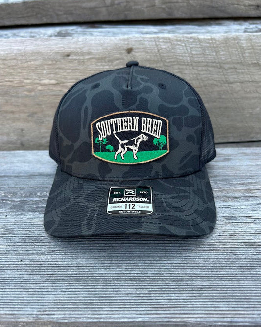 Black camouflage Richardson baseball cap with 'Southern Breed' logo and hunting dog on a wooden surface