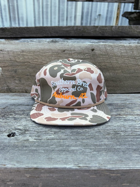 Camouflage-patterned cap with 'Southern Bred Apparel Co.' text on a wooden surface.