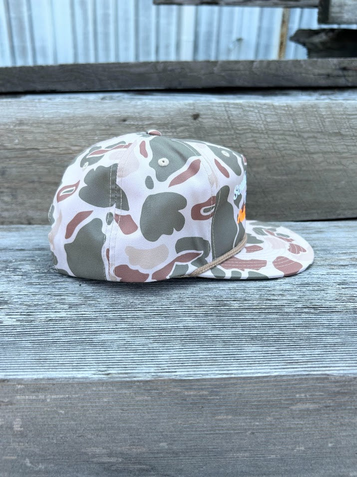 Camouflage-patterned cap on a wooden surface with a metal wall in the background