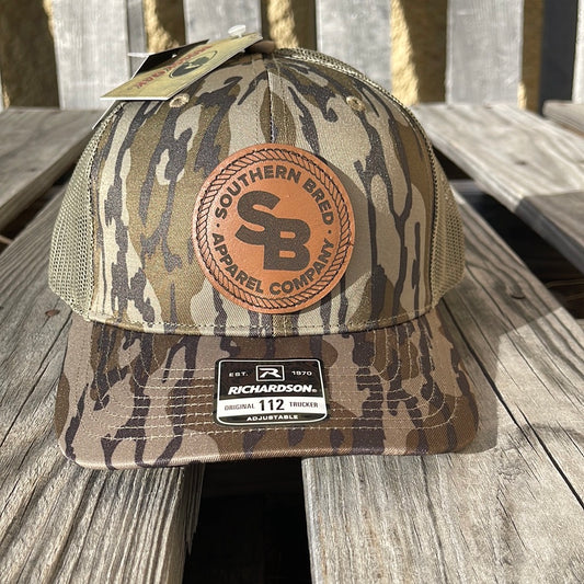 A bottomland camo pattern snapback trucker cap with a leather logo patch on the front featuring the text 'SOUTHERN BRED'.
