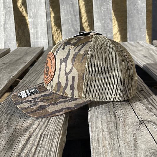 Side view of a bottomland camo pattern snapback trucker cap with a leather logo patch on the front featuring the text 'SOUTHERN BRED'.