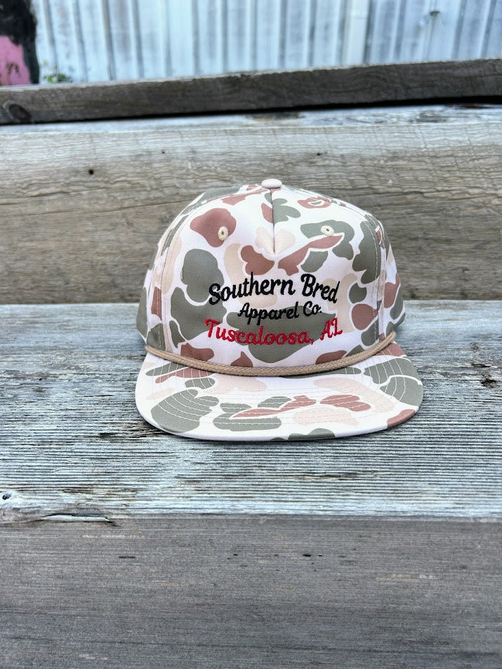 Camouflage-patterned cap with 'Southern Bred Apparel Co' text on a wooden surface