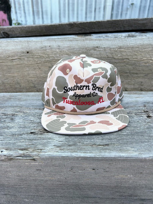Camouflage-patterned cap with 'Southern Bred Apparel Co' text on a wooden surface