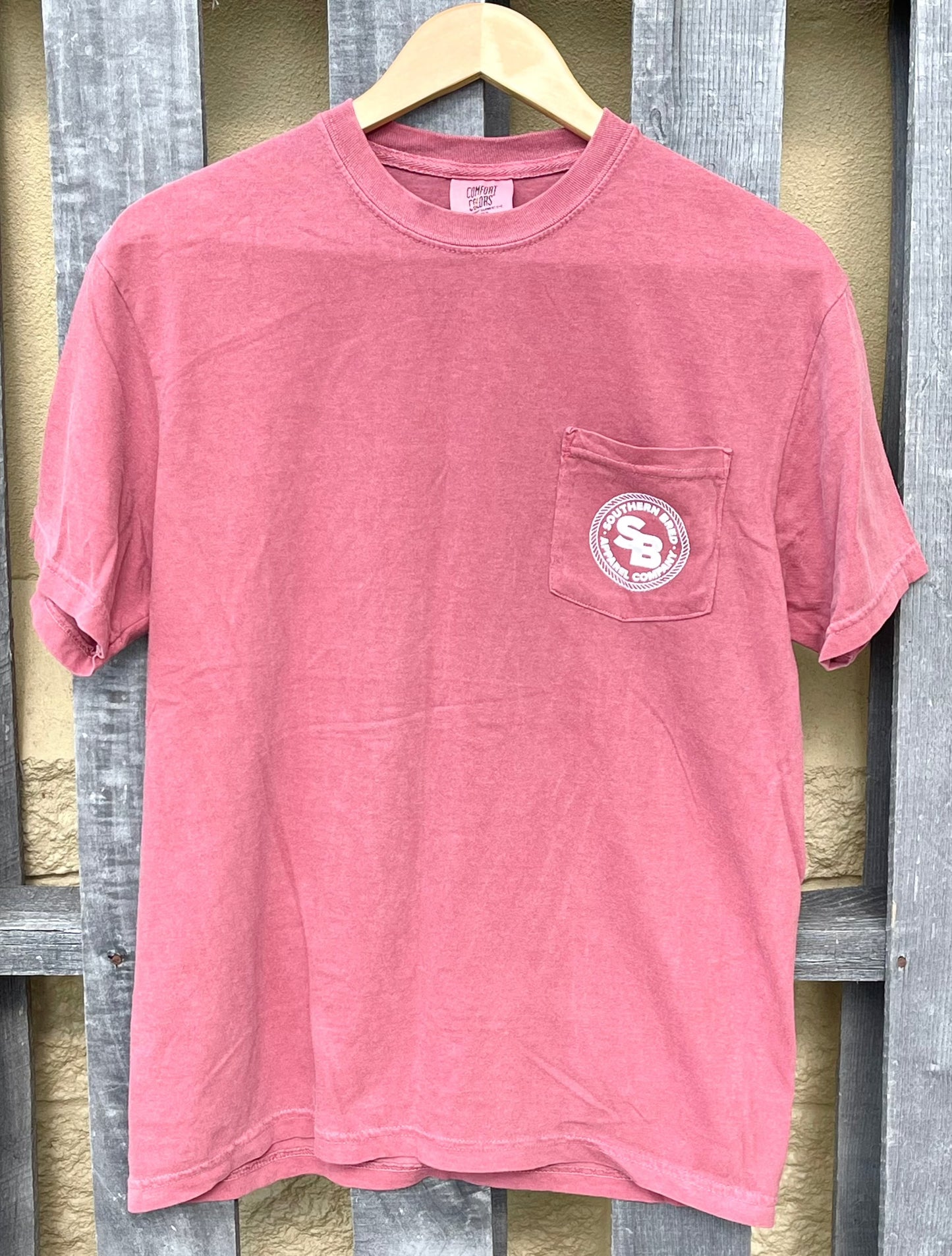 Brick t-shirt with a pocket and White logo on a wooden hanger against a wooden panel background