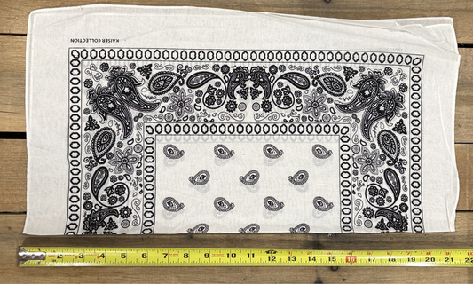 White bandana with white paisley patterns on a wooden surface, measured by a yellow tape measure.