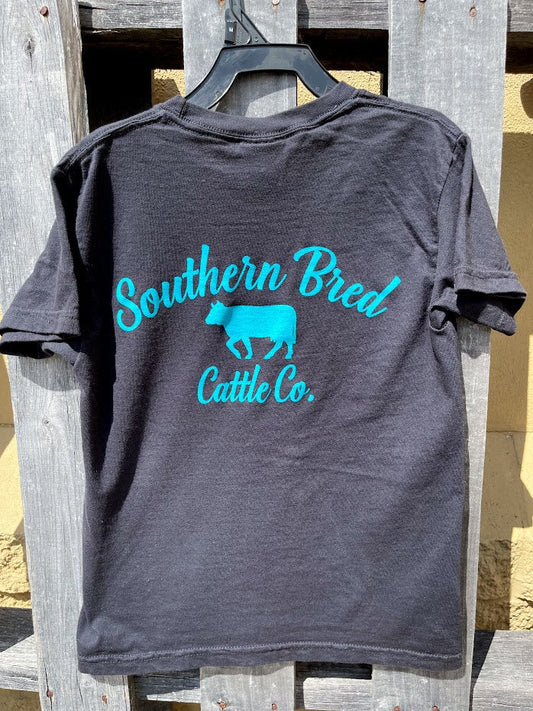 Black t-shirt with 'Southern Bred Cattle Co.' Teal text and logo on a wooden surface